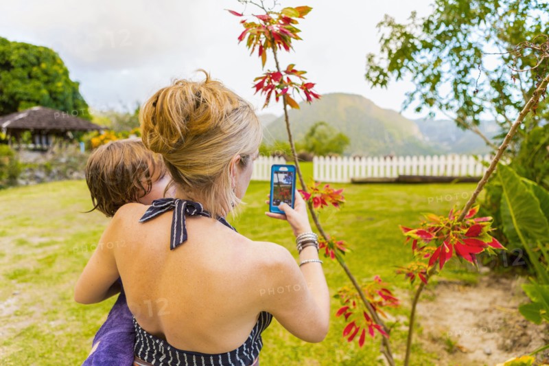 Caucasian mother carrying son and photographing with cell phone