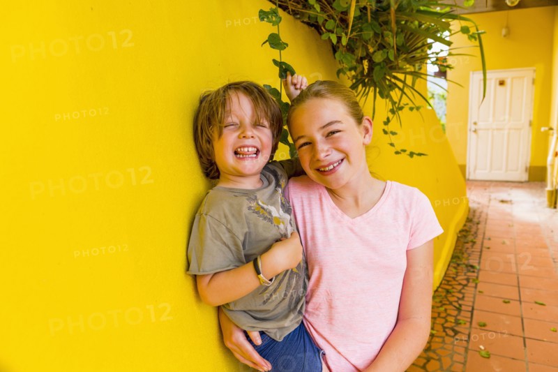 Caucasian girl leaning on yellow wall holding brother