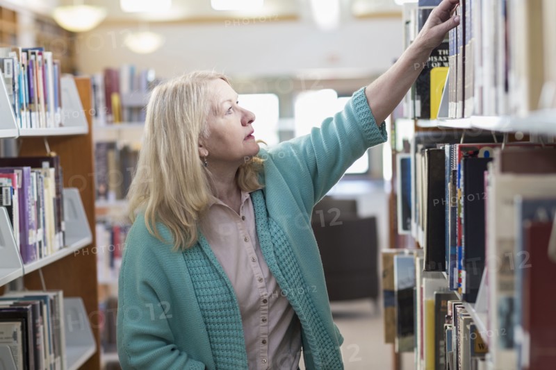 Curious Caucasian woman reaching for book in library