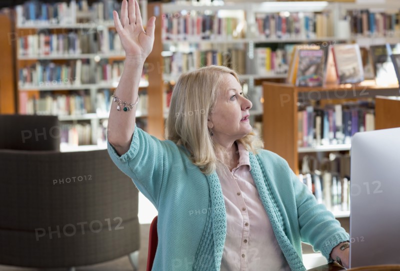 Caucasian woman using computer in library raising hand
