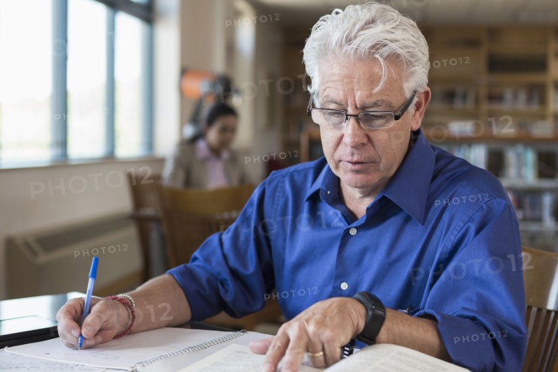 Hispanic man reading book and writing notes in library