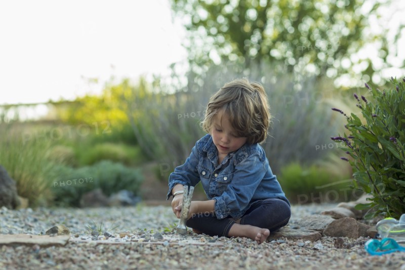 Caucasian boy sitting on ground smashing rocks with hammer