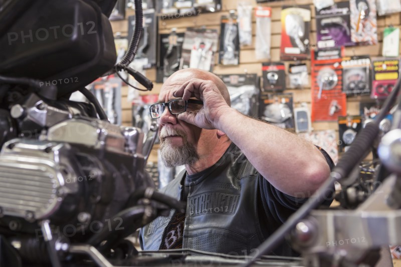 Caucasian man repairing motorcycle adjusting eyeglasses