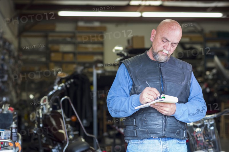 Caucasian man near motorcycle writing on notepad