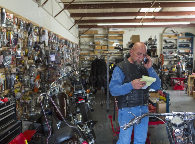 Caucasian man holding notepad near motorcycle talking on cell phone