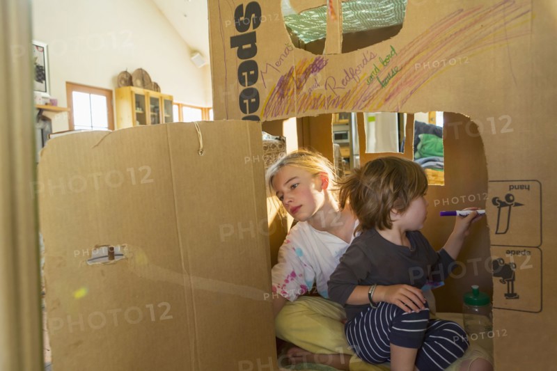 Caucasian boy and girl playing in cardboard house