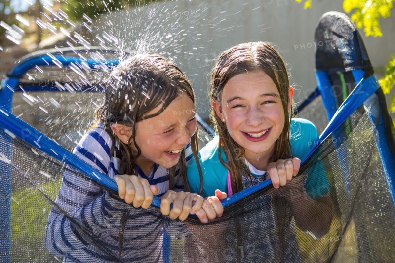 Water splashing on Caucasian girls leaning on netting