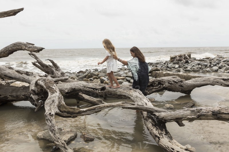 Caucasian mother and daughter walking on driftwood on beach