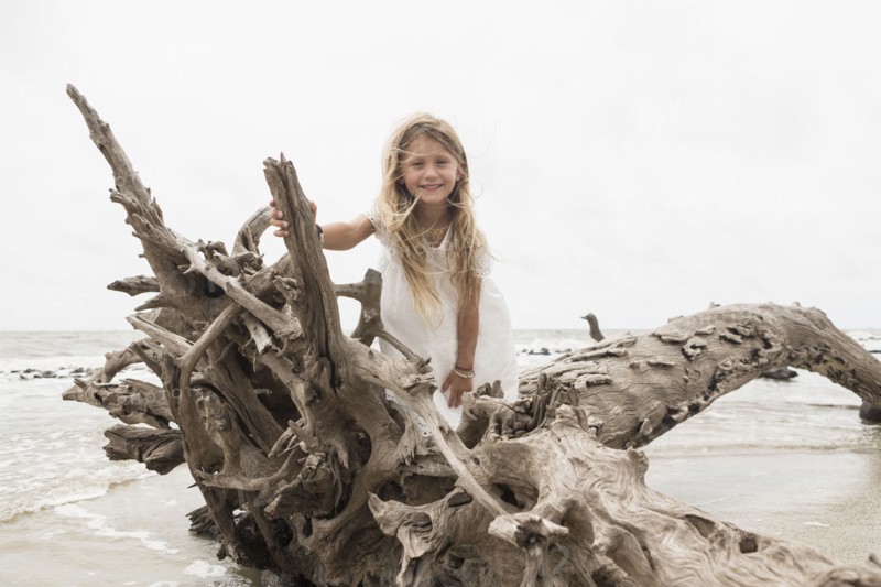 Caucasian girl posing on driftwood on beach
