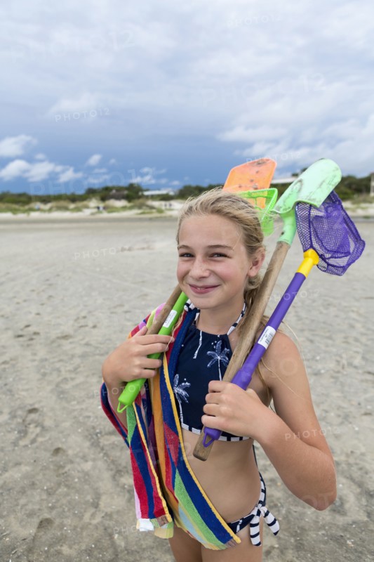 Caucasian girl on beach carrying net and shovels