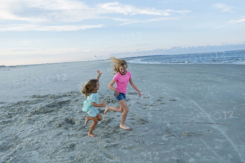 Caucasian sisters running on windy beach