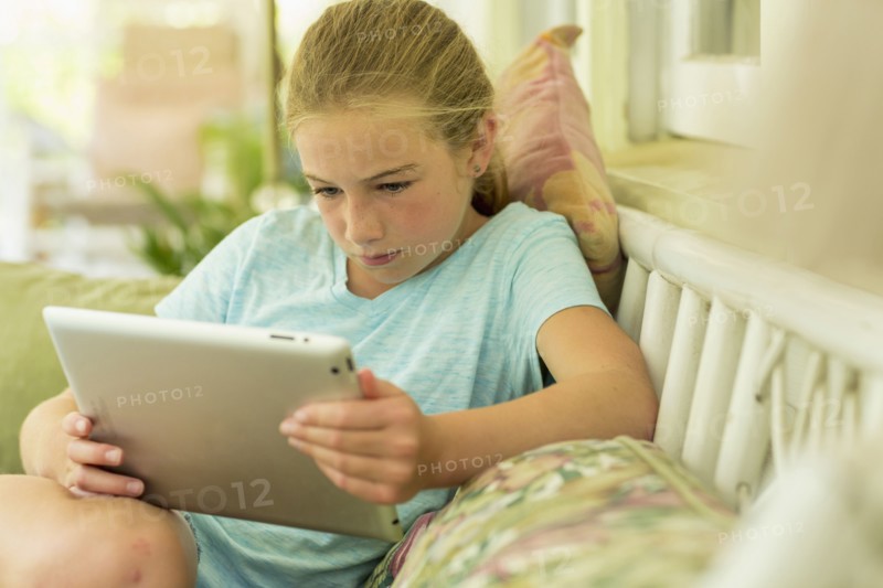 Caucasian girl sitting on sofa watching digital tablet