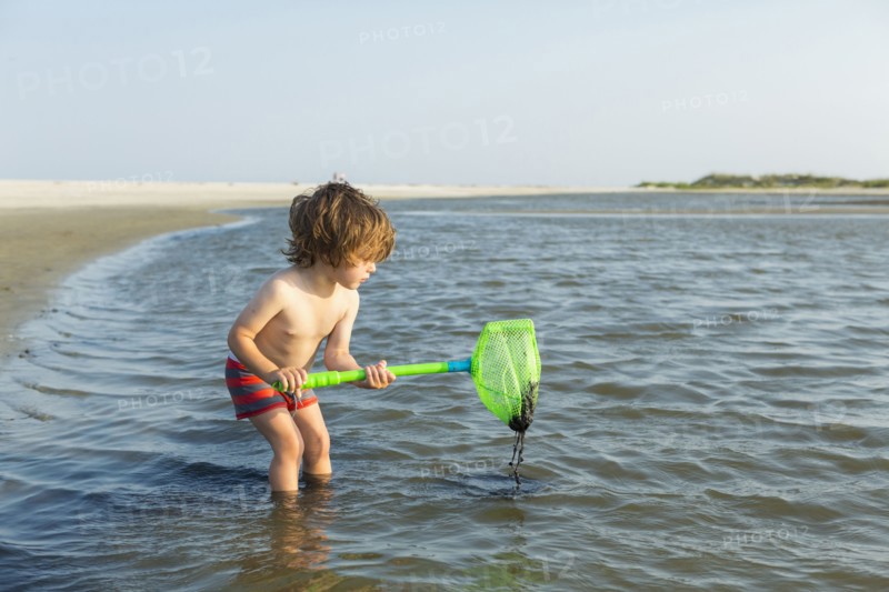 Caucasian boy wading in ocean holding