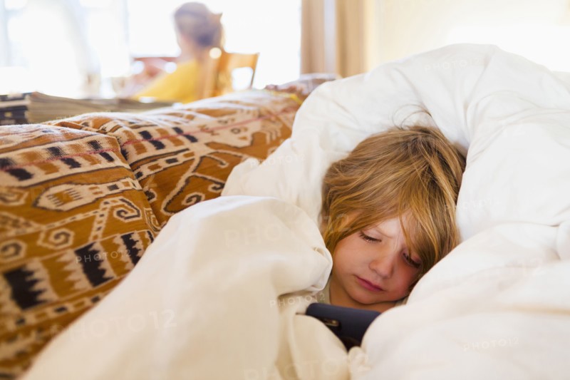 Caucasian boy laying in comforter texting on cell phone