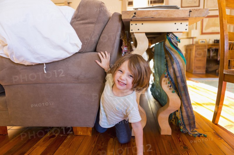 Caucasian boy crawling on floor between table and sofa