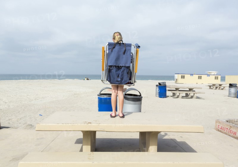 Caucasian girl carrying folding chair on picnic table at beach
