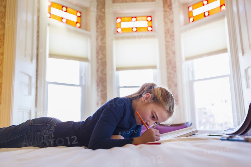 Caucasian girl laying on bed writing in notebook