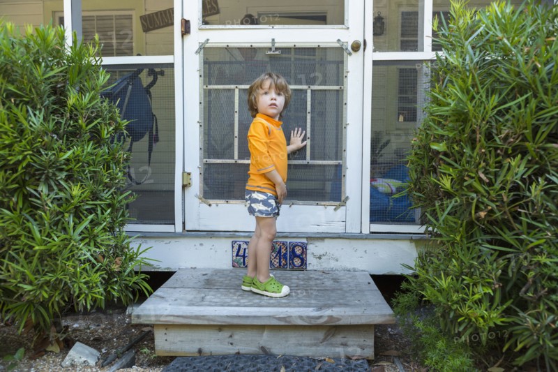 Curious Caucasian boy standing at screen door