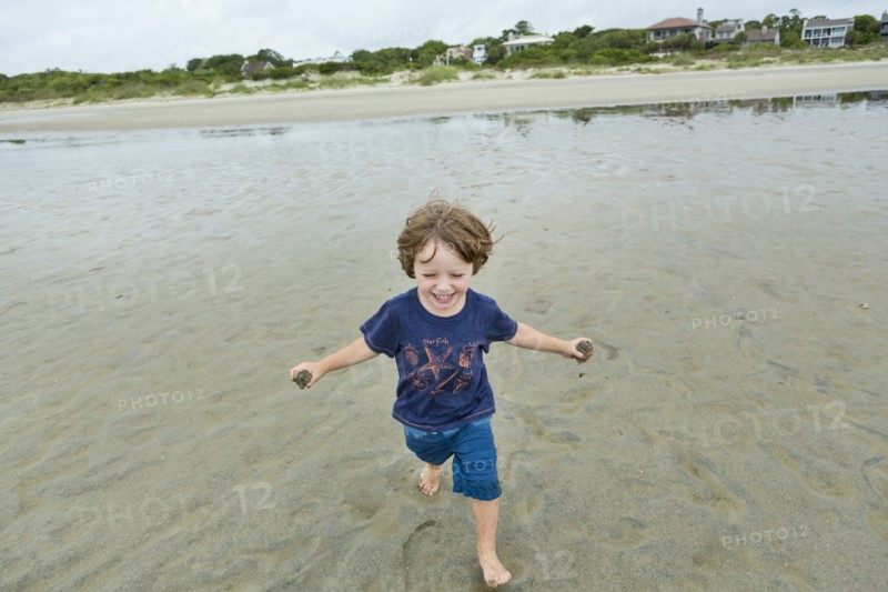 Caucasian boy running on beach carrying sand