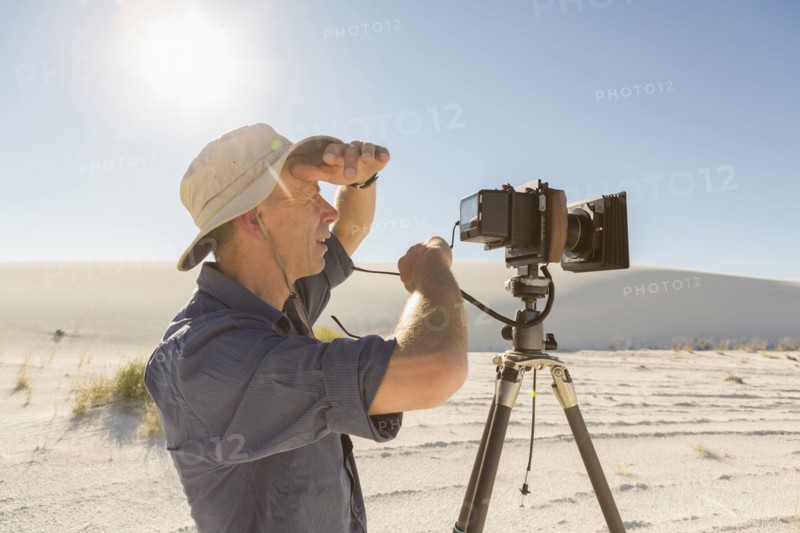 Caucasian photographer with tripod shielding eyes in desert