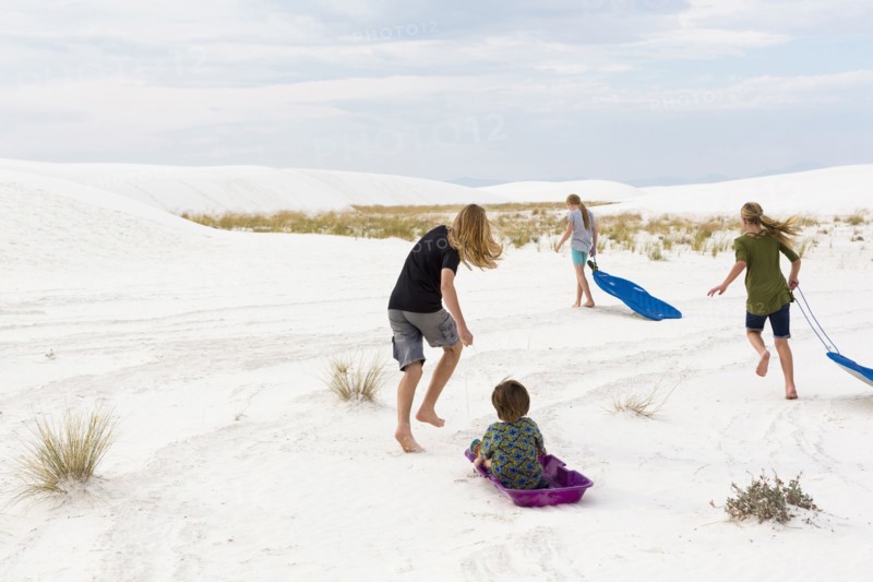 Caucasian boys and girls playing on sleds in sand