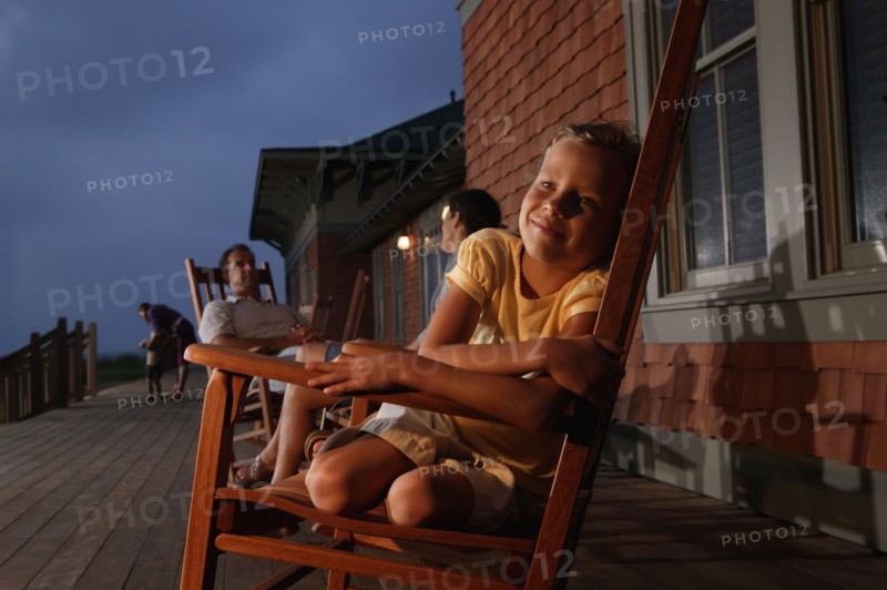 Family sitting in wooden rocking chairs at dusk