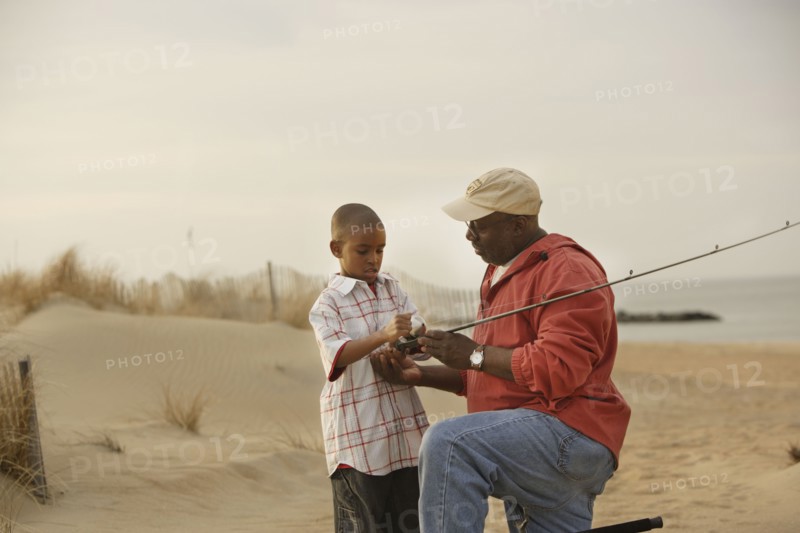 African father and son on beach with fishing gear