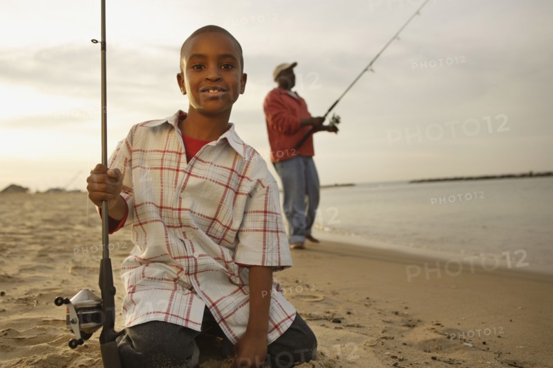 African father and son on beach with fishing gear