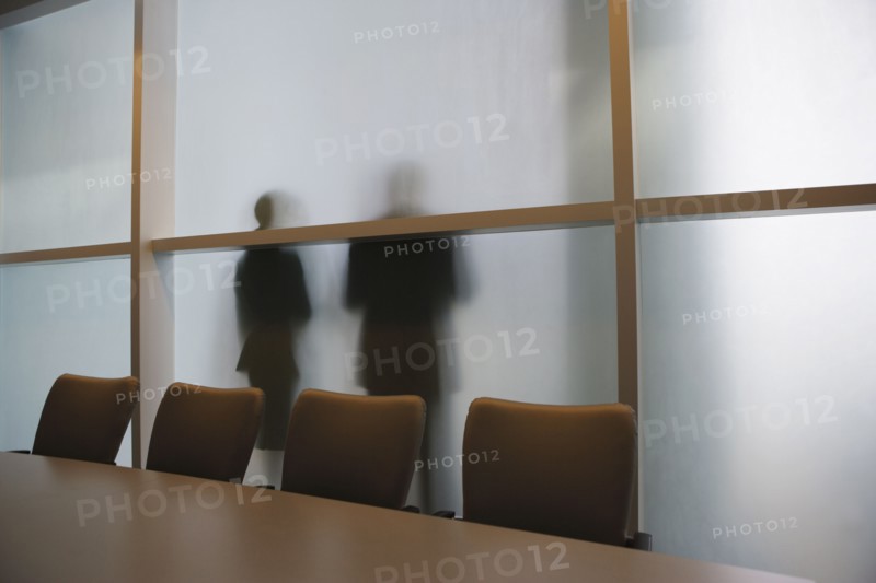 Silhouette of businesspeople through frosted glass wall