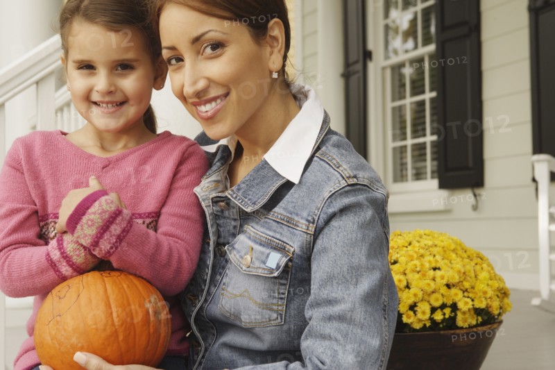 Hispanic mother and daughter holding pumpkin