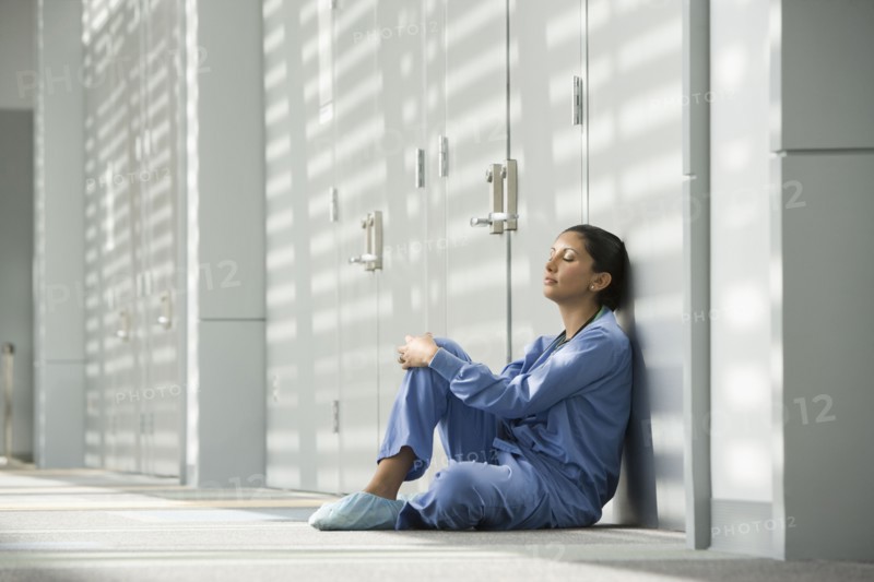 Hispanic nurse with eyes closed sitting on floor
