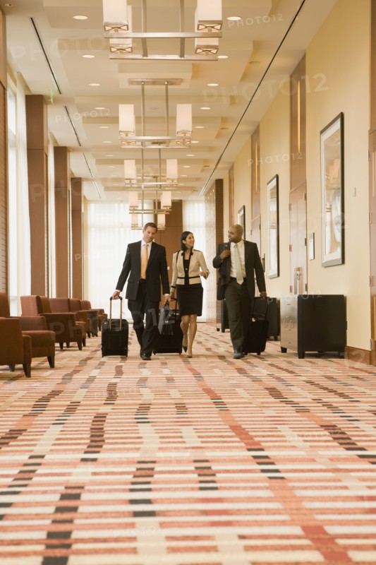 Multi-ethnic business people walking with suitcases in hotel
