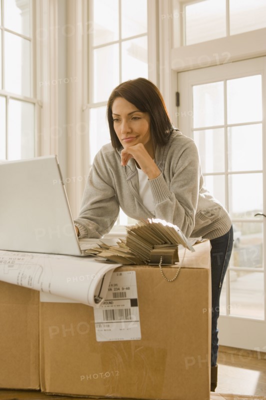 Hispanic woman using laptop on boxes