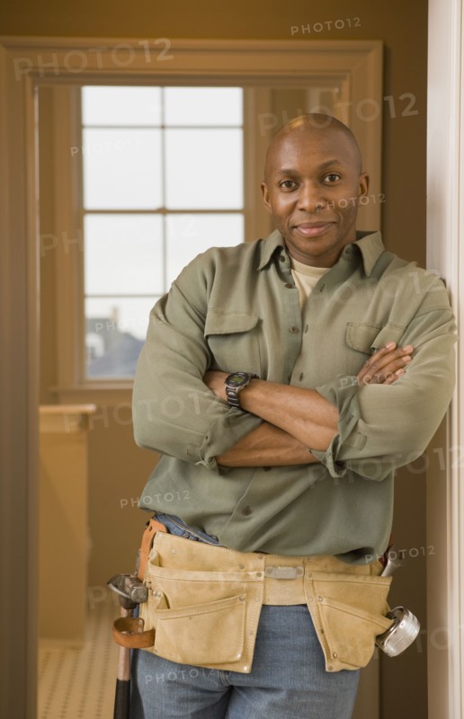 African man wearing tool belt with arms crossed