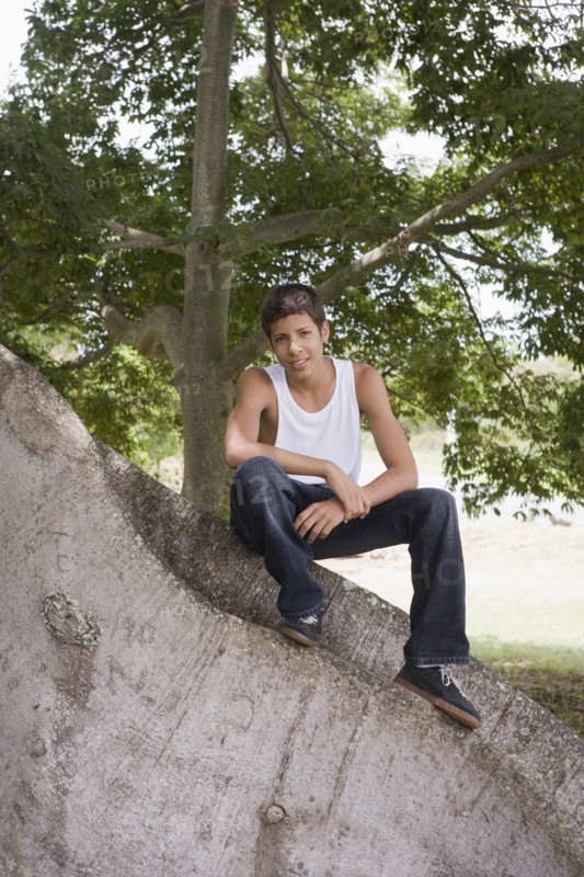 Hispanic teenager sitting on large tree trunk
