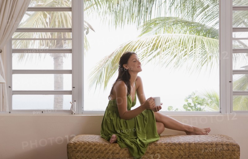 Mixed race woman drinking coffee near window