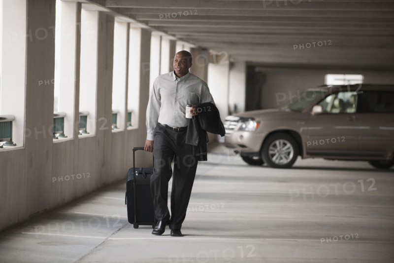 African businessman walking in parking garage with luggage