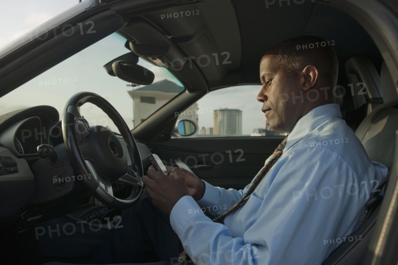 African businessman in car text messaging on cell phone