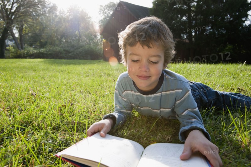 Mixed race boy reading book in grass