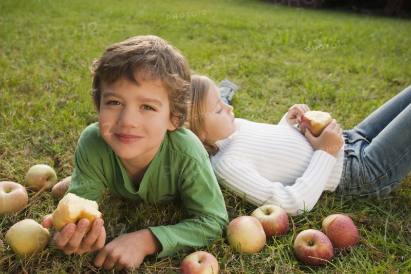 Mixed race brother and sister laying in grass with apples
