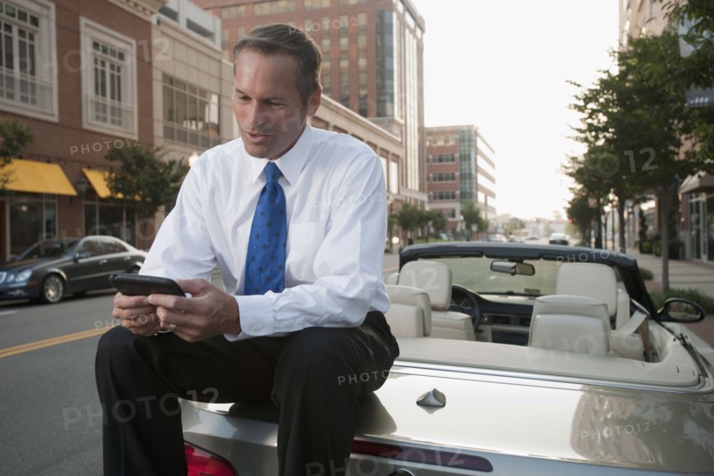 Caucasian businessman sitting on car text messaging on cell phone