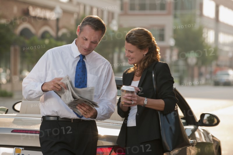 Caucasian business people looking at newspaper