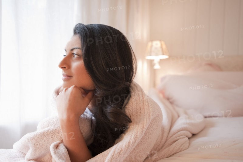 Middle Eastern woman laying on bed thinking