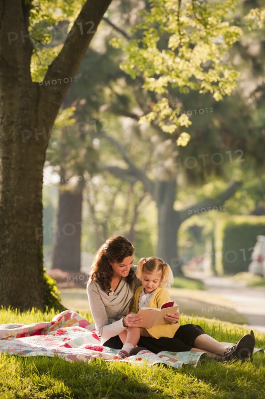 Caucasian mother reading story to daughter in park