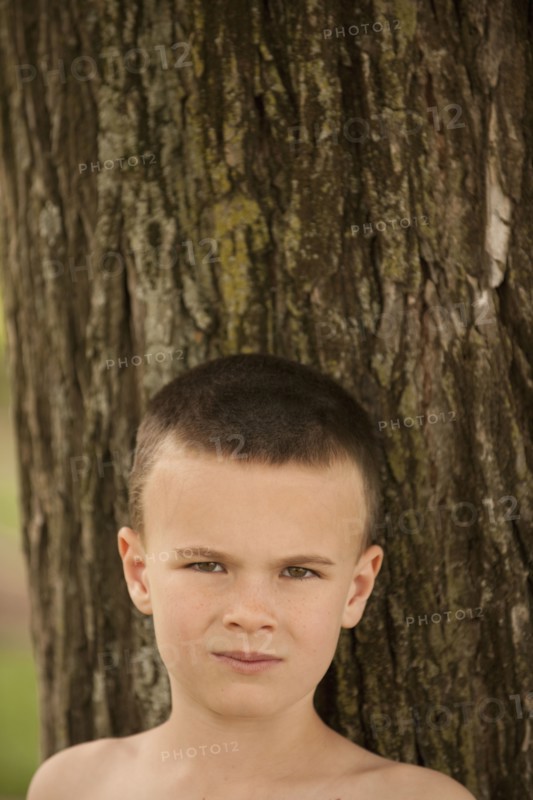 Caucasian boy leaning against tree trunk