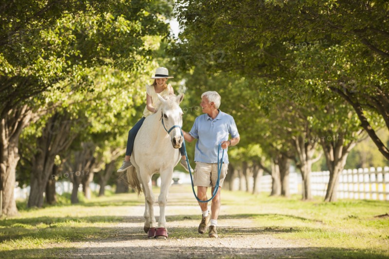 Caucasian man walking horse with granddaughter