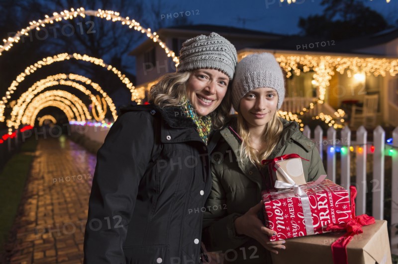 Caucasian mother and daughter holding Christmas gifts on sidewalk