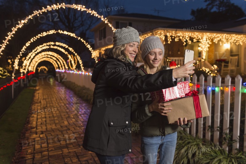 Caucasian mother and daughter holding Christmas gifts posing for selfie