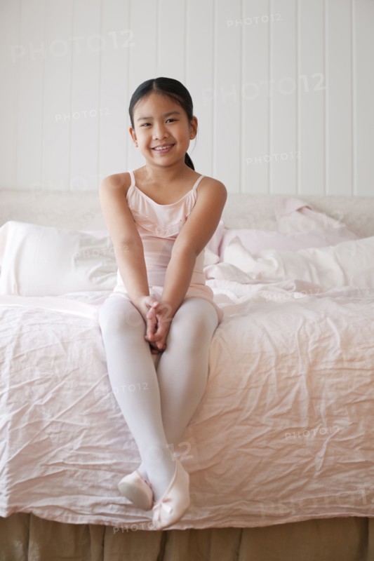 Asian girl in ballet costume sitting on bed