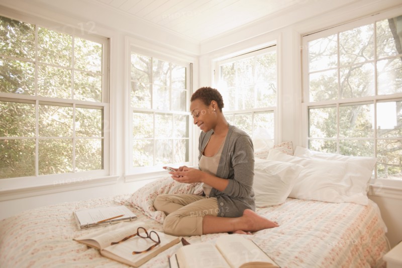 African American woman studying in bed and using cell phone